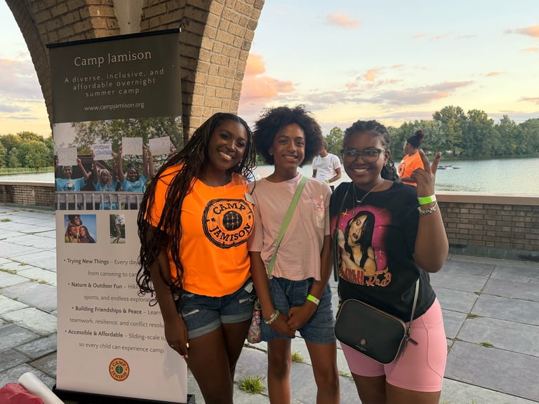 Three young people smiling at Camp Jamison by a waterfront at sunset with trees in the background