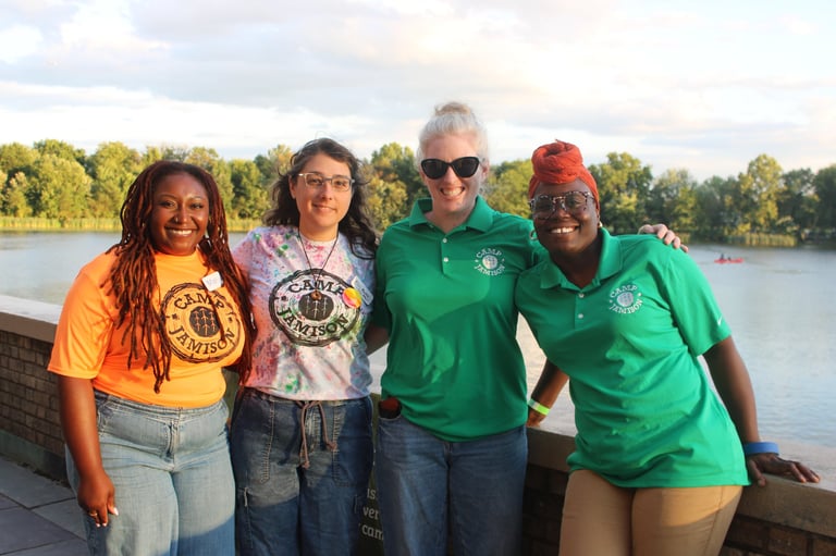 Jacqueline McDonough with Camp Jamison Board and Staff together by the river holding a sign, smiling at the camera