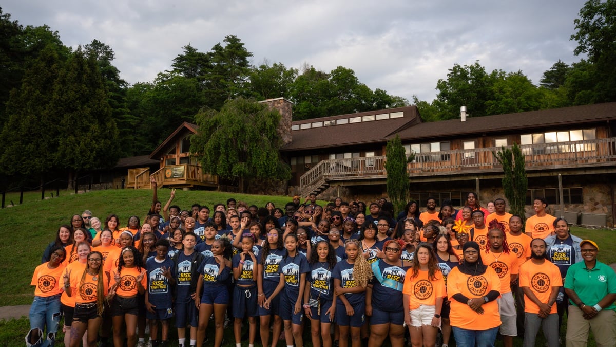 Large group of people wearing yellow and blue shirts posing together outdoors in front of a brick building and trees